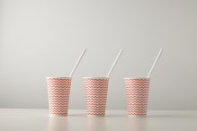 retail set three paper cups decorated with red line pattern with white drinking straw inside isolated white table