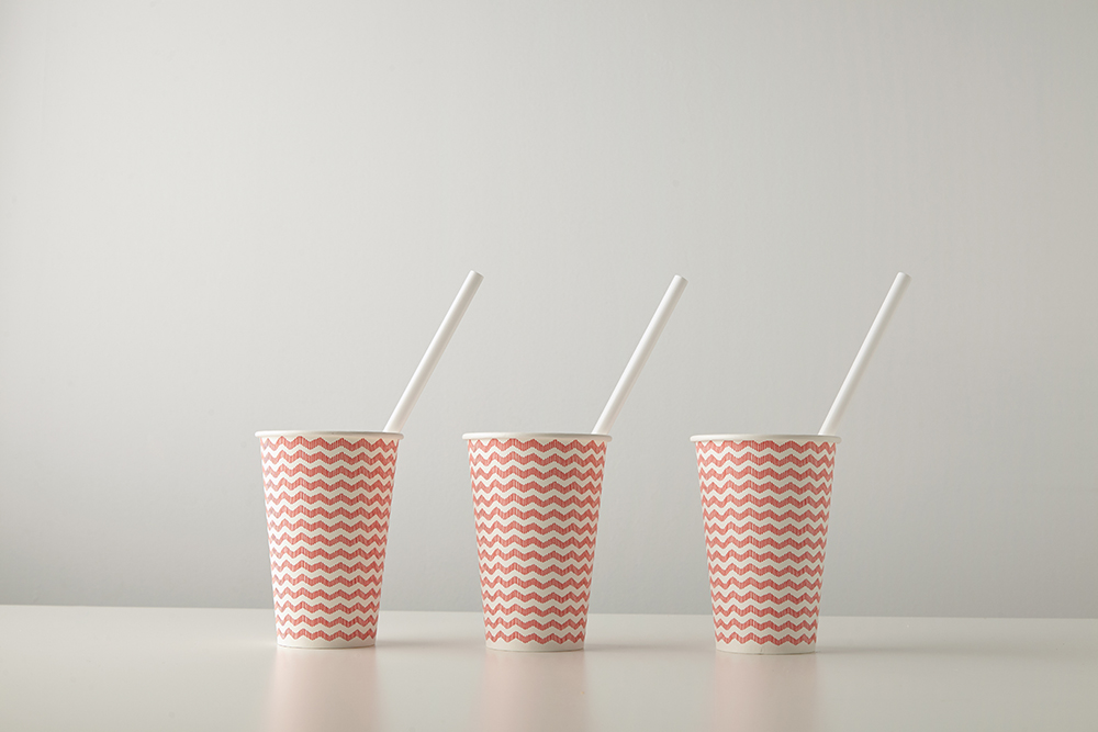 Retail set of three paper cups decorated with red line pattern and with white drinking straw inside isolated on white table Place for your text above