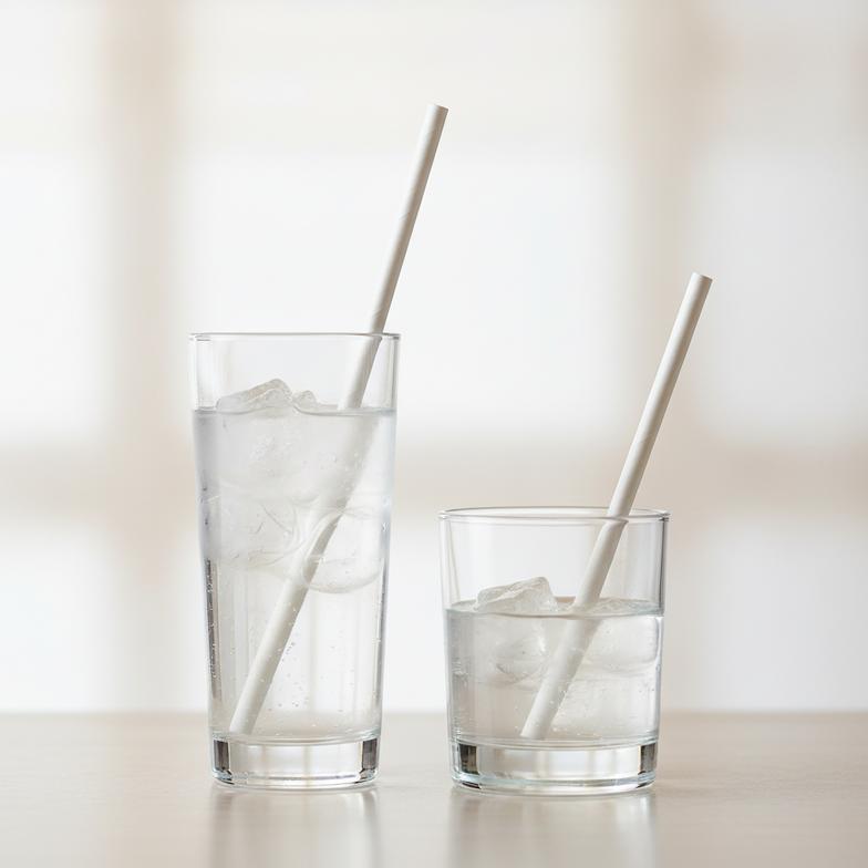 Different sizes of cocktail paper straws next to highball and lowball glasses