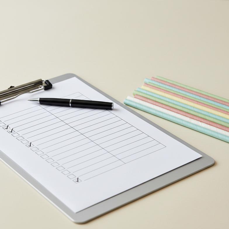 A checklist on a clipboard next to a stack of colored paper straws.