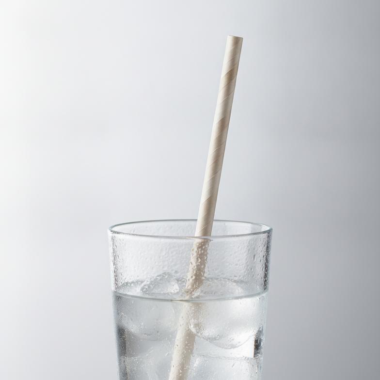 A durable paper straw standing perfectly straight in a glass of water after several hours, demonstrating its anti-sog properties.