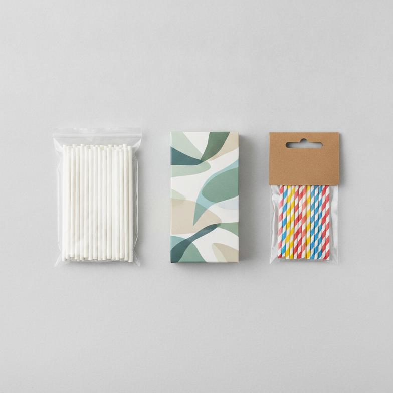 An assortment of paper straw packaging options including a polybag, a retail paper box, and a stack of straws with a header card.