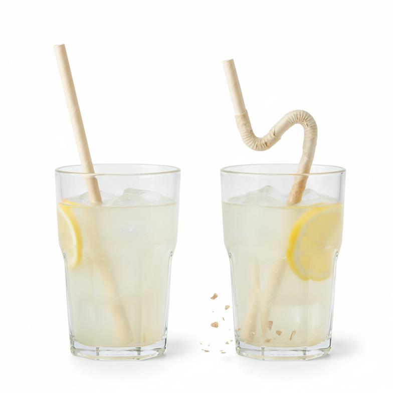 A durable paper straw holding its shape in a glass of lemonade next to a standard straw that is unravelling.