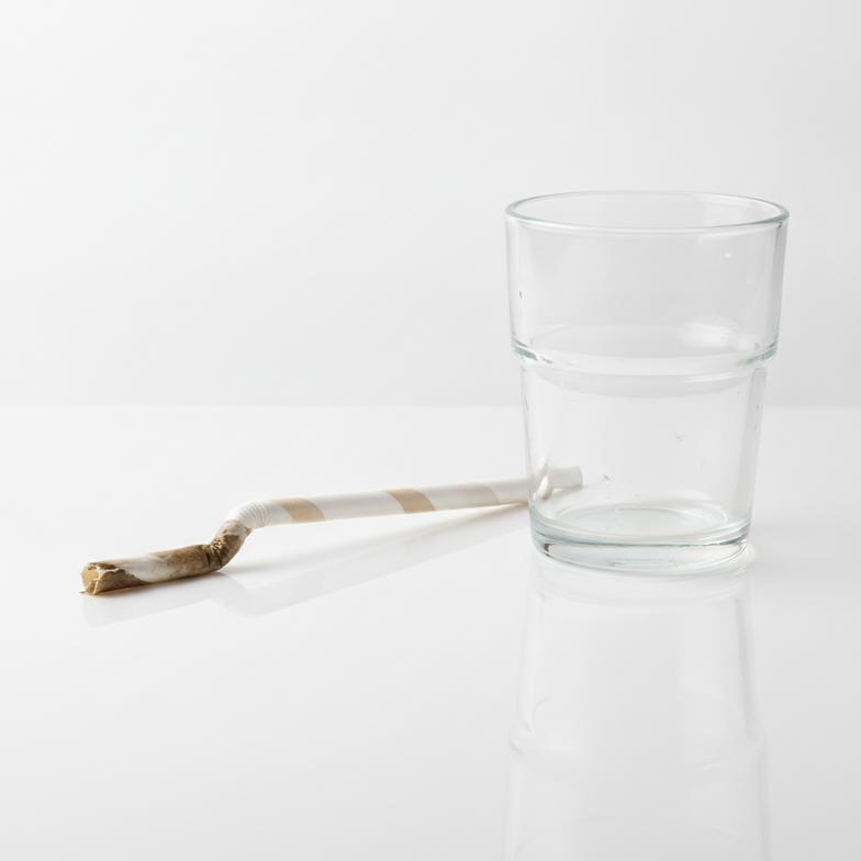 A soggy, failed paper straw next to a glass, demonstrating poor paper straw stability.