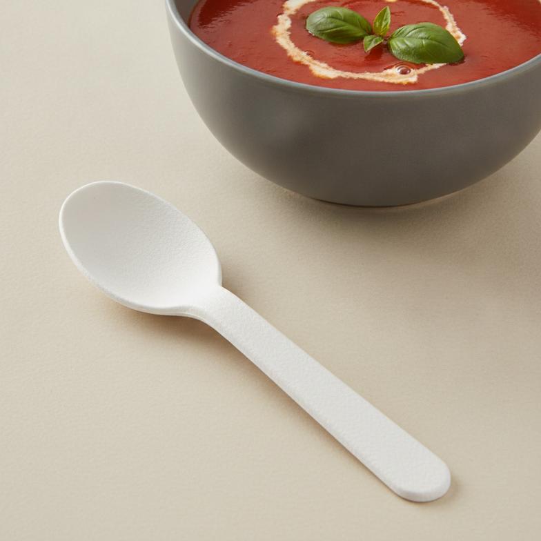 A high-quality paper spoon next to a cup of hot soup, demonstrating its durability.