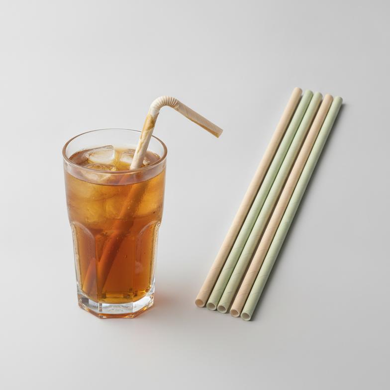 A collection of durable, high-quality paper straws next to a glass of iced tea, illustrating why paper straws become soft when not made correctly.