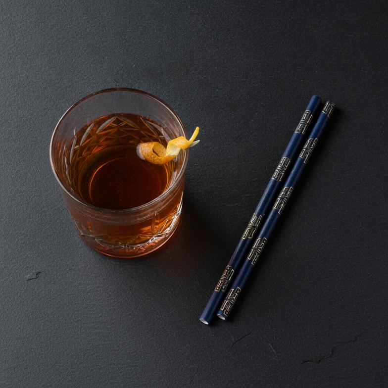 Custom-branded paper cocktail straws with a bar's logo next to an elegant cocktail.