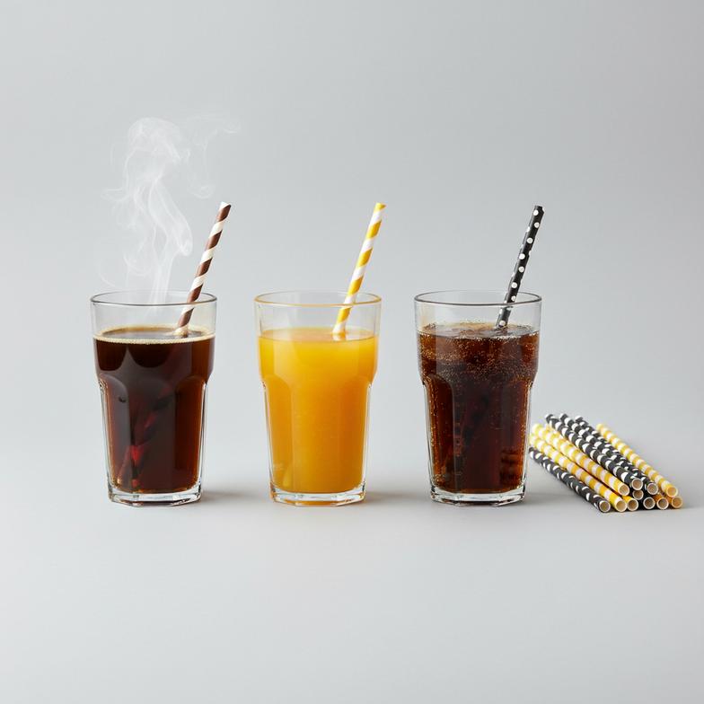 A collection of paper straws with different patterns sitting next to various drinks like coffee, soda, and juice.