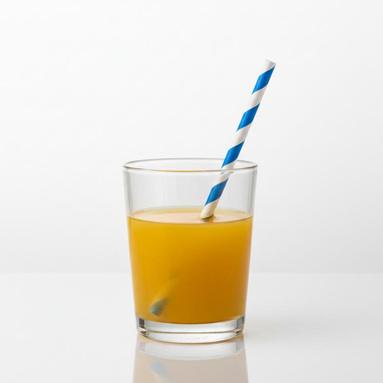 A paper straw in a glass of orange juice, visibly starting to soften at the bottom.